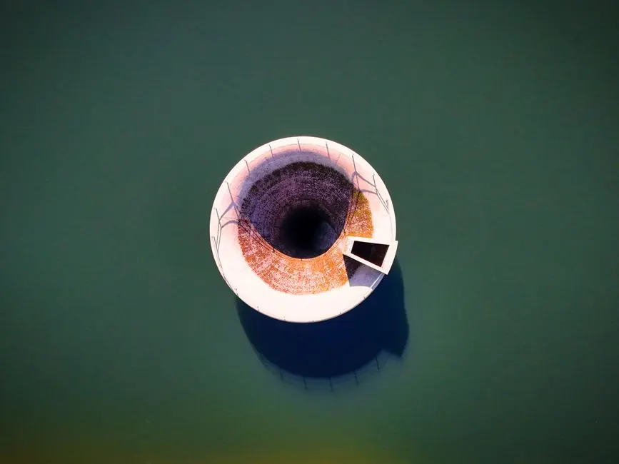 Aerial view of a bell mouth spillway in a calm reservoir, highlighting engineering and architecture.