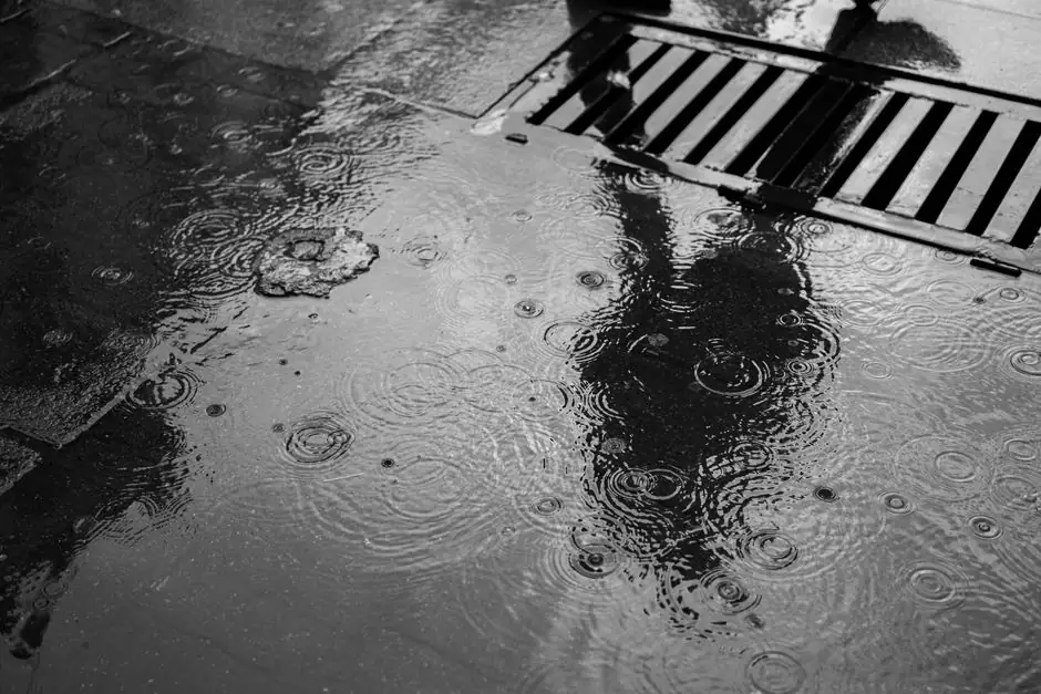 Moody monochrome image of a pedestrian's reflection on a rainy street surface.