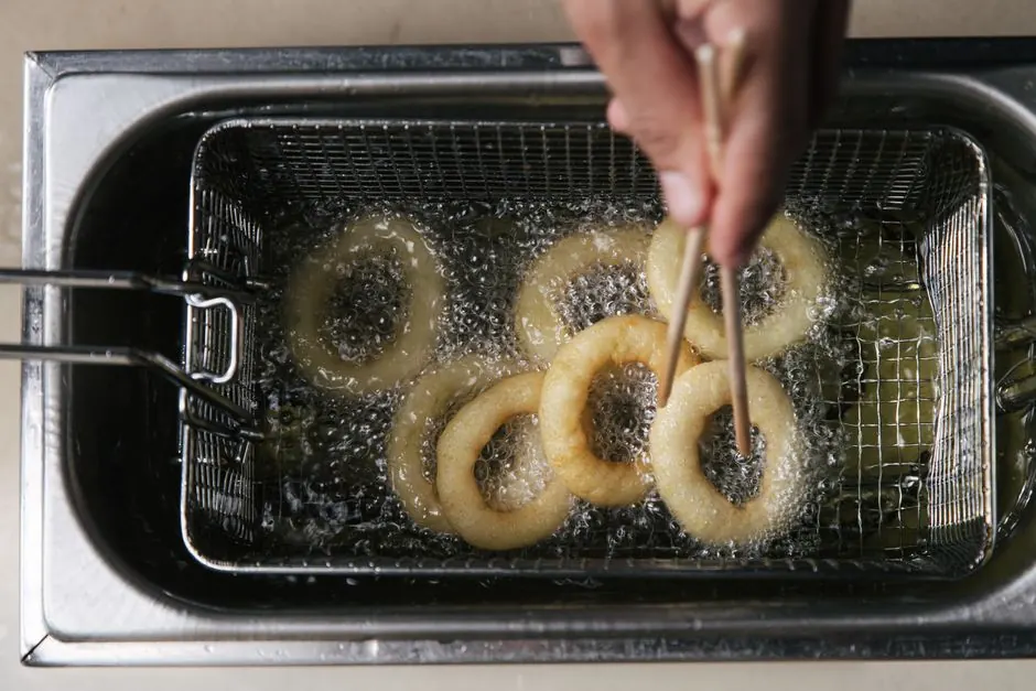 Overhead view of onion rings frying in hot oil with chopsticks in a deep fryer.